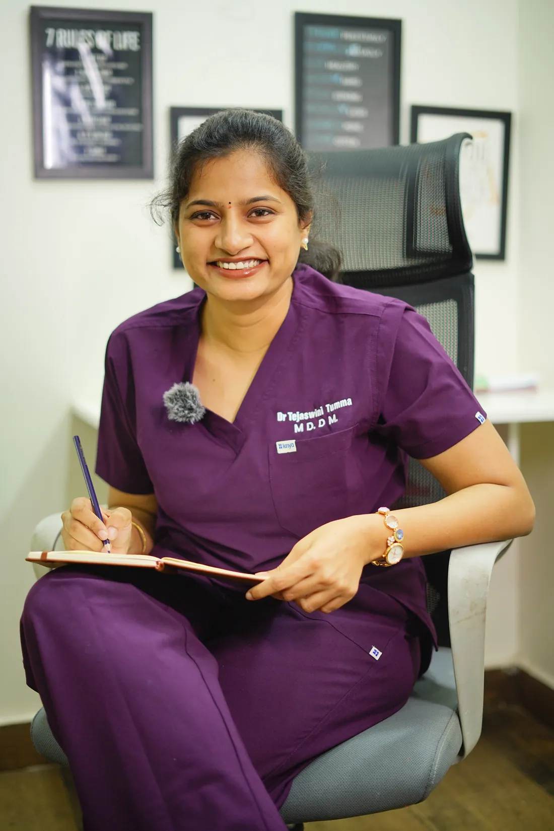 Dr. Tejaswini Tumma smiling at her desk in the clinic, writing in a notebook